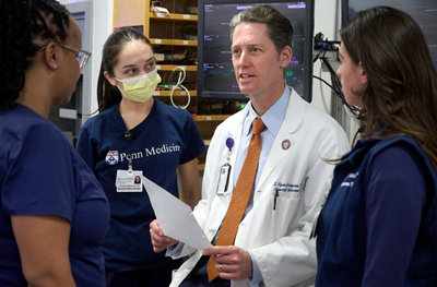 Dr. S. Ryan Greysen, in white coat, speaks to three nurses in scrubs.